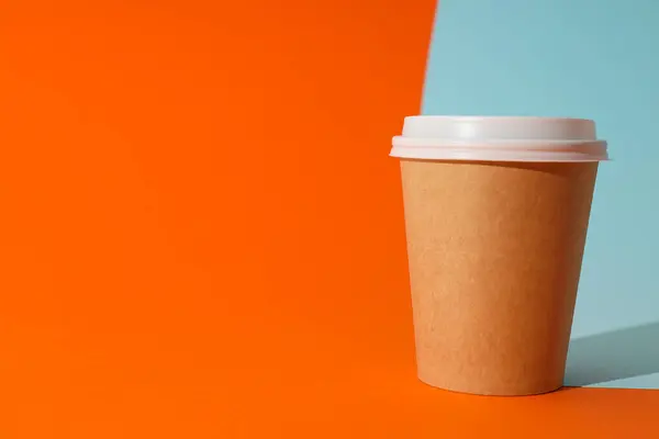 A paper cup with a lid on an orange background