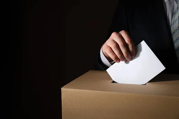Paper box and hand with voting paper on dark background, space for text