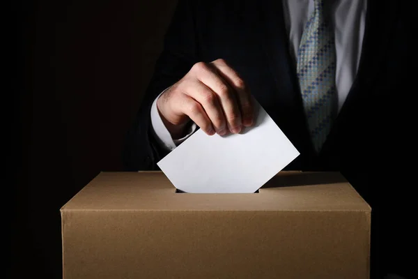 Paper box and hand with voting paper on dark background, close up