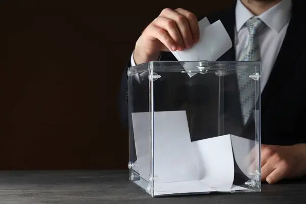 Transparent box with voting papers and man in suit on brown background, space for text
