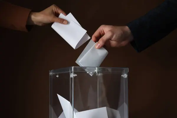 Transparent box and hands with voting papers on brown background