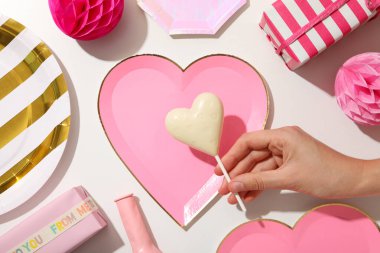 Elinde beyaz çikolata, hediye kutuları ve beyaz arka planda tabaklar, üst manzara.