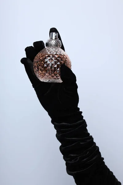A bottle of perfume in a gloved hand.