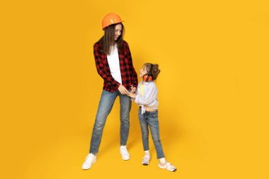 Anne ve kızı inşaat için aksesuarlarla, sarı arka planda..