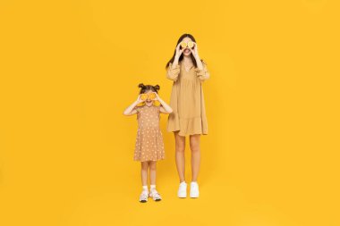 Anne ve kızı sarı arka planda oynuyorlar..