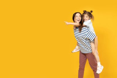 Anne ve kızı sarı arka planda oynuyorlar..