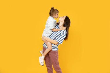 Anne ve kızı sarı arka planda oynuyorlar..