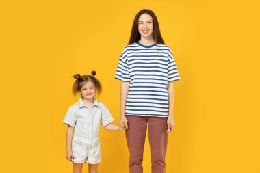 Anne ve kızı sarı arka planda bir fotoğraf için poz veriyor..