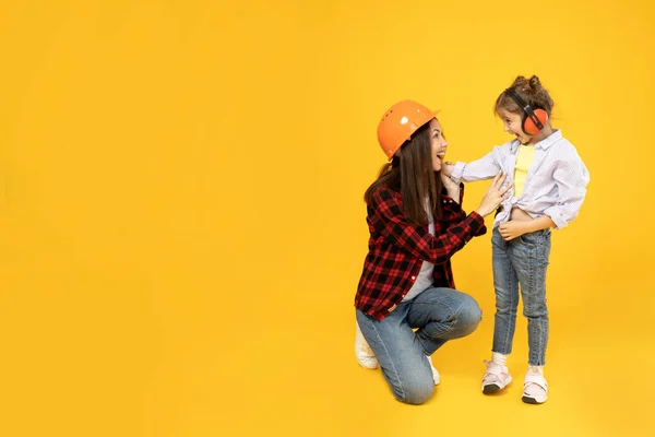 Mother and daughter in accessories for construction, on a yellow background.