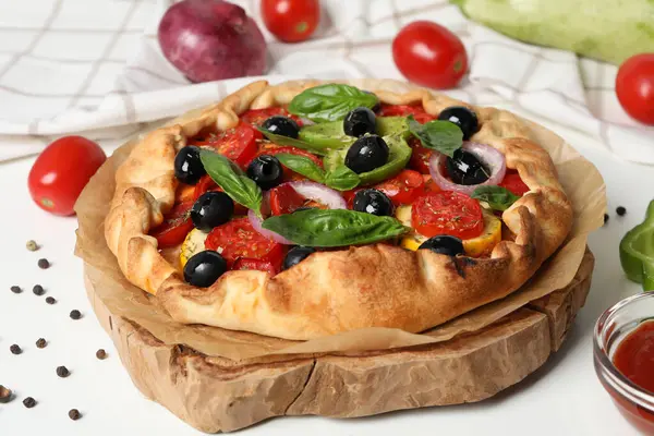 Freshly baked vegetable galette with fresh vegetables on a white background