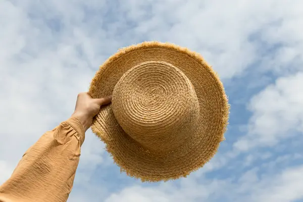A straw hat in his hand, against the background of the sky.