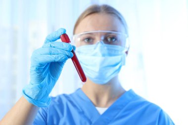 Laboratuvar asistanı elinde donör kanı olan bir deney tüpü ile mavi arka planda.