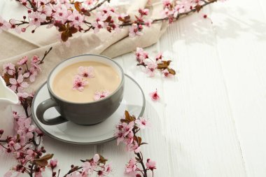 Çiçekli bahar dalları, bir bardak sıcak içecekle, açık ahşap arka planda..