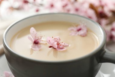 Çiçekli bahar dalları, bir bardak sıcak içecekle, açık ahşap arka planda..