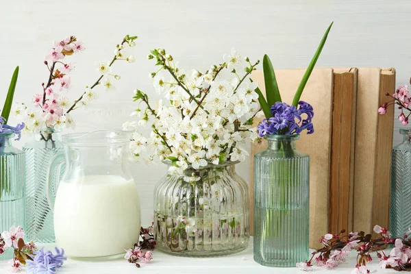 Kavanozda çiçekli bahar dalları, arka planda hafif kitaplarla.