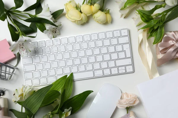 Keyboard and flowers with a shopping cart, on a light background.