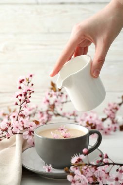 Çiçekli bahar dalları, bir bardak sıcak içecekle, açık ahşap arka planda..