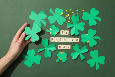 Elinde kağıt yonca yaprakları, altın sikkeler ve yeşil arka planda harfler, üst manzara.