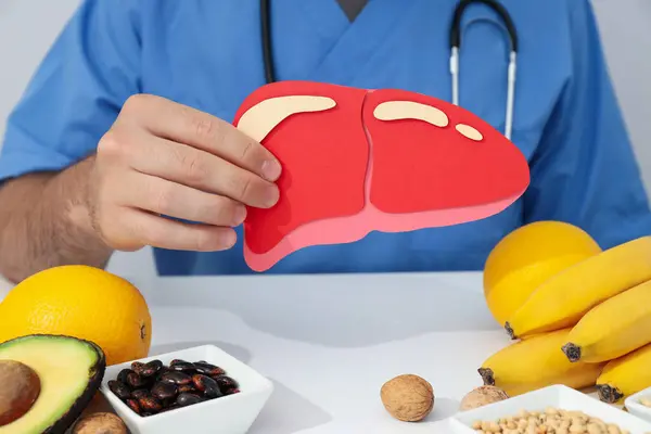 Paper liver in the doctor\'s hand, fruits and beans on light background, close up