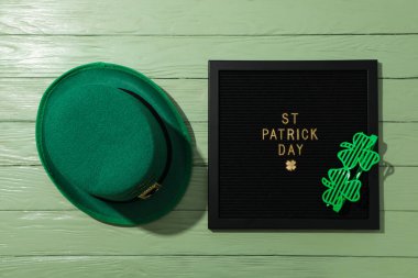 Yeşil ahşap zemin üzerinde metin, gözlük ve yeşil şapka olan siyah harf tahtası, üst görünüm