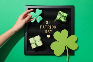 Üzerinde altın harfler olan siyah harfler, ellerinde yonca yaprakları ve yeşil arka planda hediye kutuları.