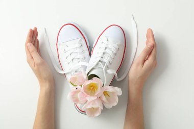 Beyaz arka planda kadın ayakkabılarında eller ve çiçekler, üst manzara.