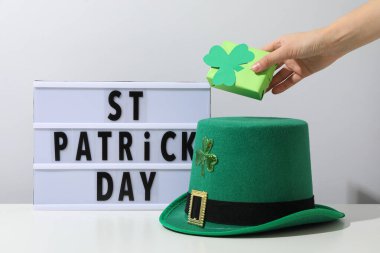 Elinde yeşil hediye kutusu, beyaz arkaplanda yazı olan şapka ve ışık kutusu.