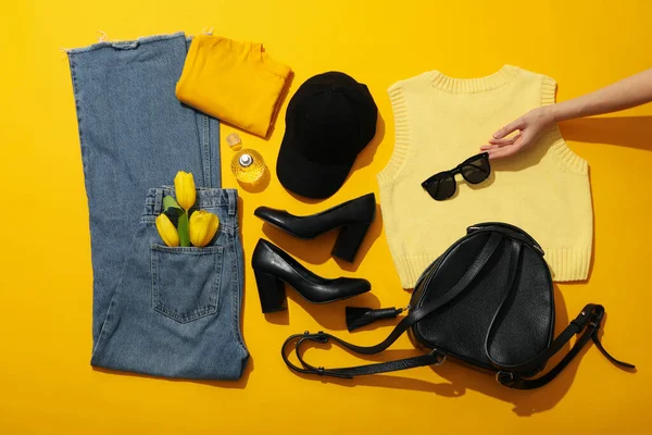 Female clothes, shoes, accessories and hand on yellow background, top view