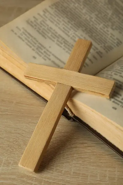 Wooden cross on book on wooden background, close up
