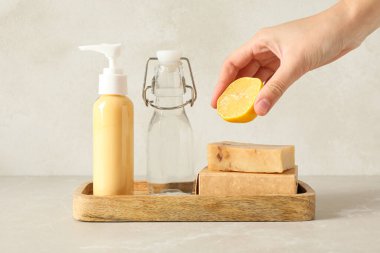Deterjanlı şişeler, elinde limon ve arka planında sabun kalıpları.
