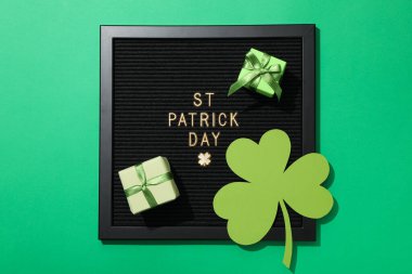 Üzerinde altın harfler, kağıt yonca yaprağı ve yeşil arka planda hediye kutuları olan siyah harfler.