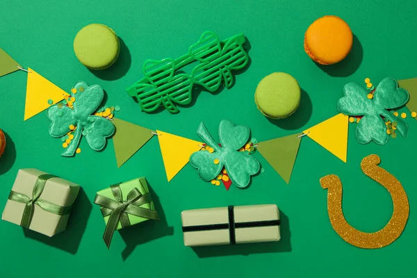 Yonca yaprakları, kağıt bayraklar, hediye kutuları ve kurabiyeler yeşil arka planda, üst manzara