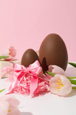 Arkaplanda hediyeler ve çiçekler olan çikolata yumurtası.