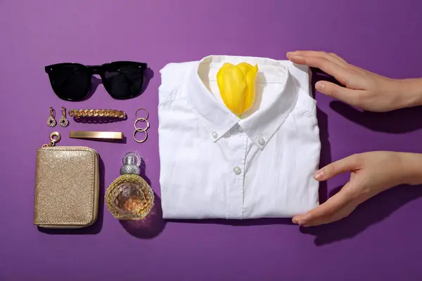 Female shirt, hands and accessories on purple background, top view