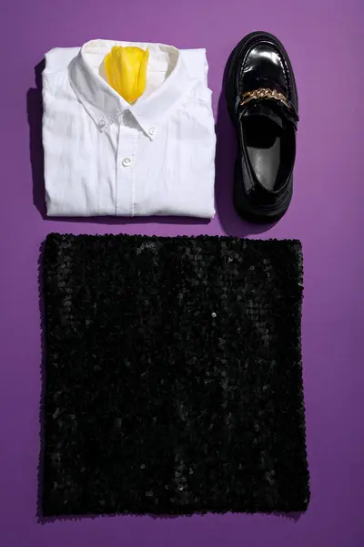 Female shirt, skirt and loafers on purple background, top view
