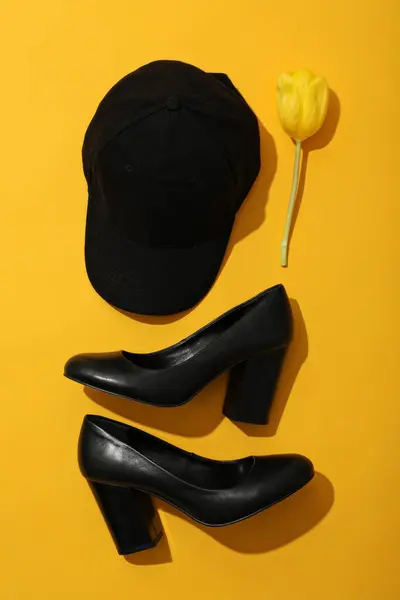 Black cap, shoes and tulip on yellow background, top view