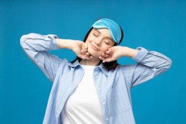 Mavi arka planda, uyku maskeli genç bir kadın.