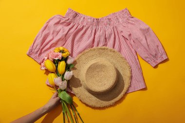 Sarı arka planda kadın bluzu, şapka ve çiçekler, üst manzara.