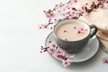 Çiçekli bahar dalları, bir bardak sıcak içecekle, açık ahşap arka planda..