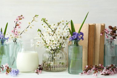 Kavanozda çiçekli bahar dalları, arka planda hafif kitaplarla.