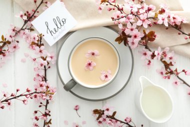 Çiçekli bahar dalları, bir bardak sıcak içecekle, açık ahşap arka planda..