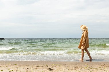 Yazın sahilde, elbiseli bir kız yürüyor..