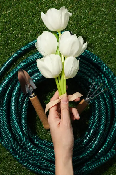 Garden supplies and tulips in hand on green background, top view