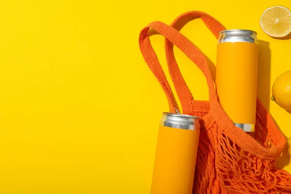 Tin cans in yellow labels in string bag, lemons on yellow background, space for text