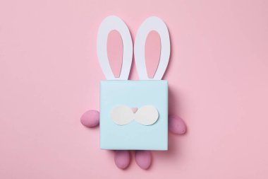 Pembe arka planda tavşan kulaklı mavi hediye kutusu