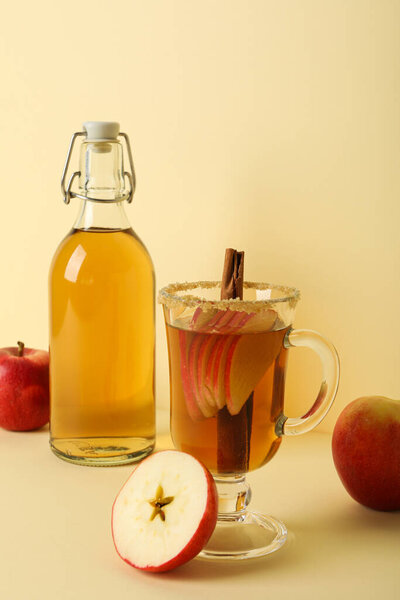 Glass cup and bottle with apple cider and red apples on beige background