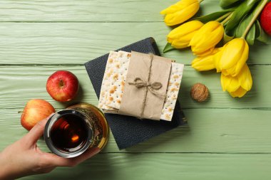 Matzo, elinde kupa, yeşil ahşap arka planda elmalar ve çiçekler, üst manzara.