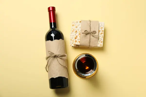 Bottle of wine, cup and matzo on light yellow background, top view
