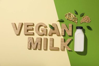 Alternatif süt şişesi ve bej ve yeşil arka planda ahşap harfler.