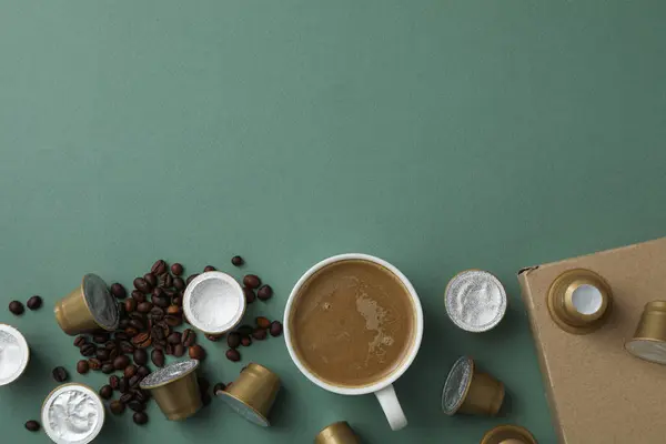Coffee capsules, beans, cup with coffee drink and box on green background, space for text